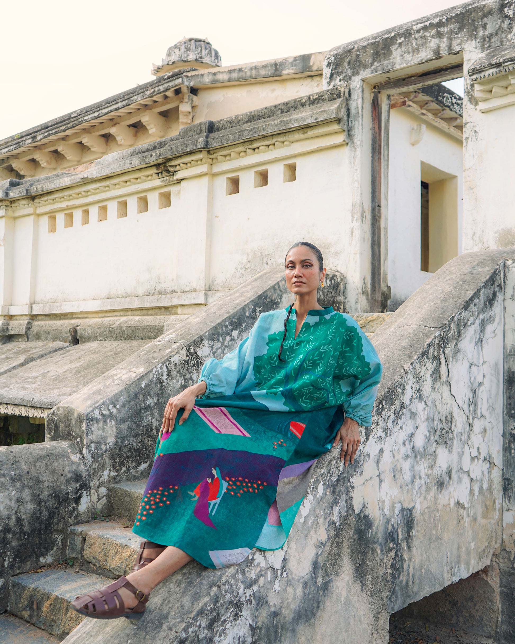 Woman in a colorful dress sitting on stone steps with classical architecture in the background