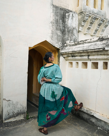 Woman in a teal dress standing in an architectural setting with white walls and a textured roof.