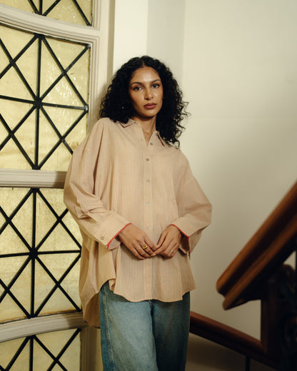 Woman wearing a beige Oversized Shirt - Sand Striped and blue jeans standing indoors.