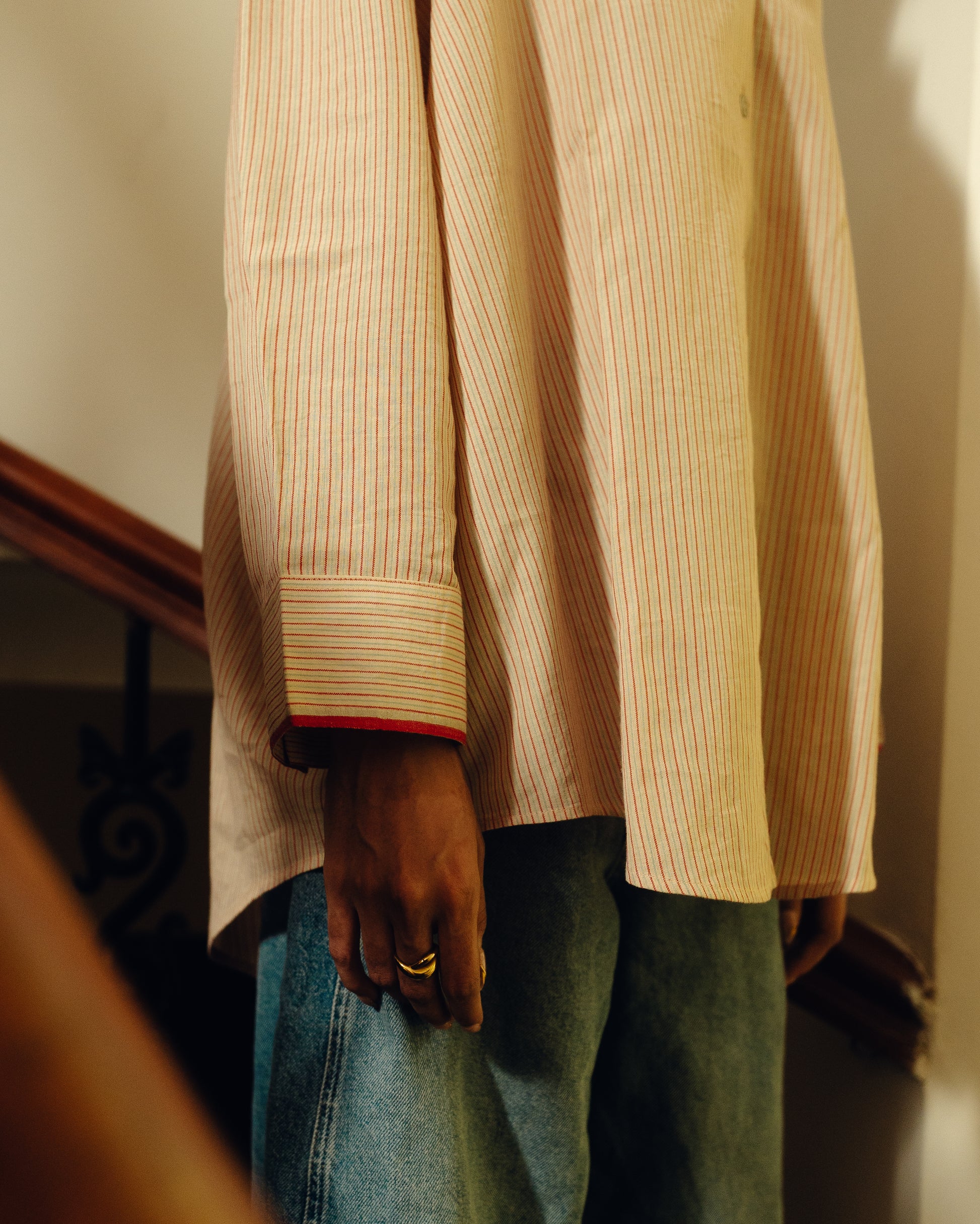 Person wearing a beige striped Oversized Shirt - Sand Striped and blue jeans with a blurred background