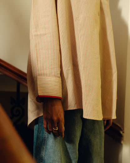 Person wearing a beige striped Oversized Shirt - Sand Striped and blue jeans with a blurred background