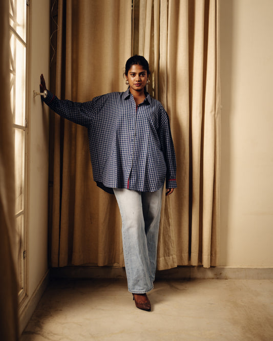 Person wearing a Oversized shirt - Blueberry checks and light jeans standing in a room with beige curtains.