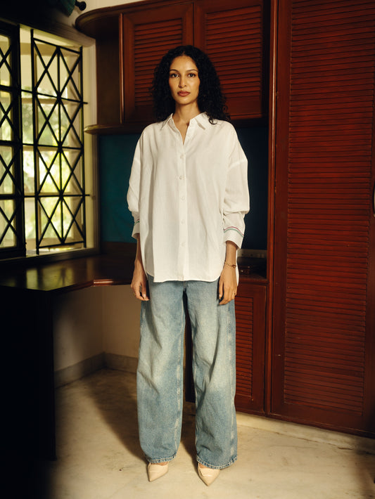 Woman wearing a Oversized shirt - White and blue jeans standing in a room with wooden shutters.