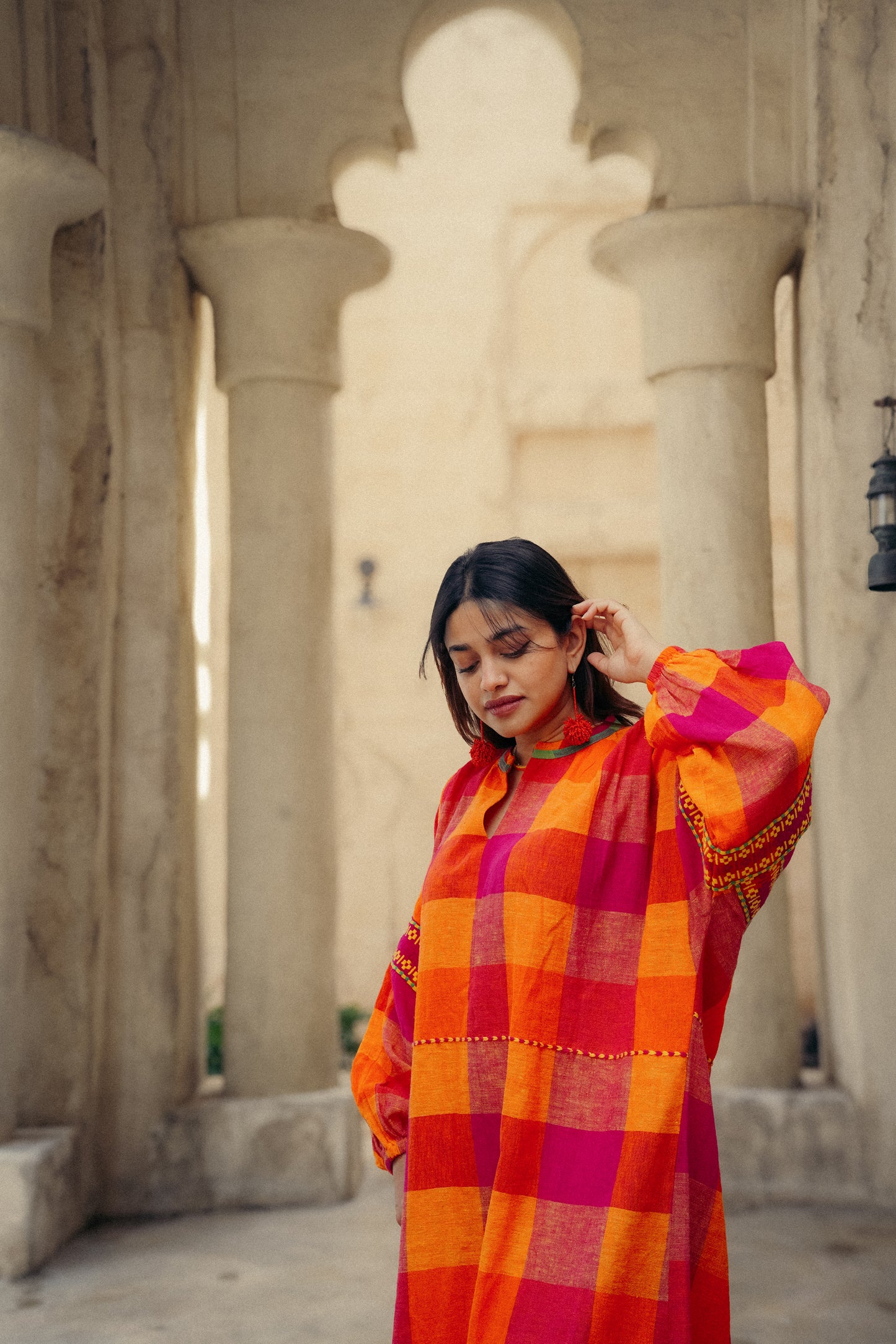 Woman wearing a vibrant orange and red checkered dress in an architectural setting.