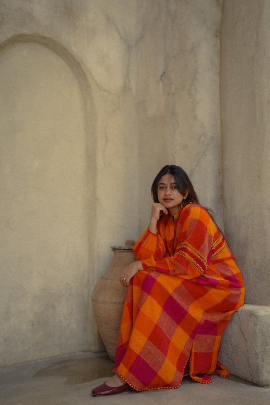 Woman in a colorful dress sitting against a textured wall.