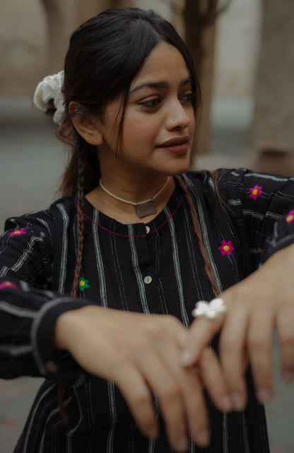 Woman wearing a black outfit with floral patterns, holding a small object.