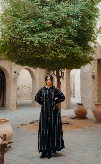 Woman in a black dress standing in an outdoor courtyard with trees and stone arches.