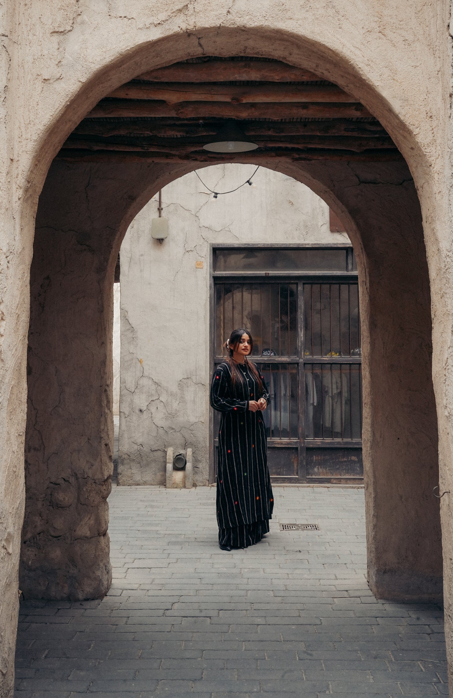 Woman in a long black dress standing under a stone archway.