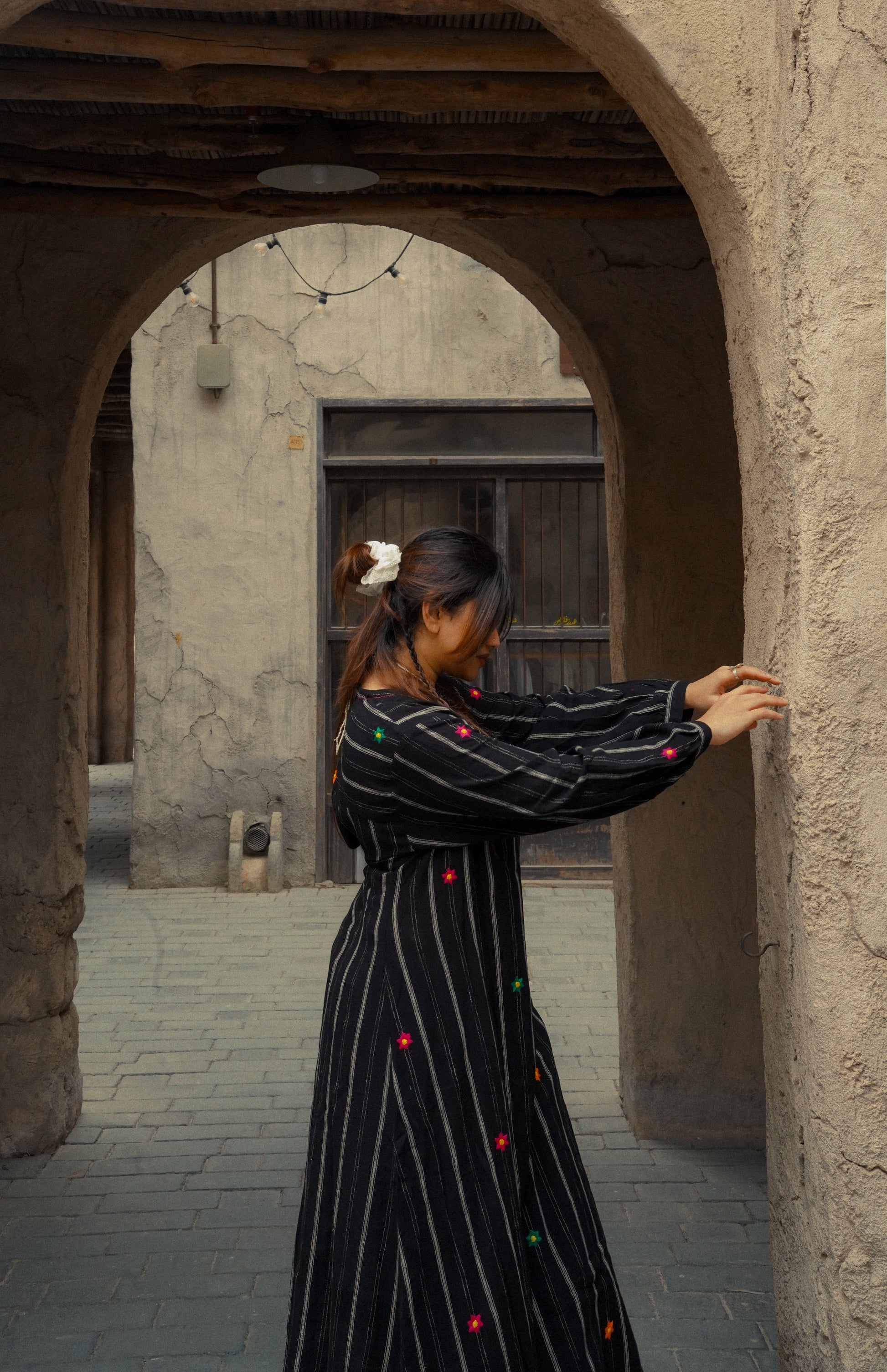 Woman in a black dress with colorful buttons standing in an arched stone doorway.