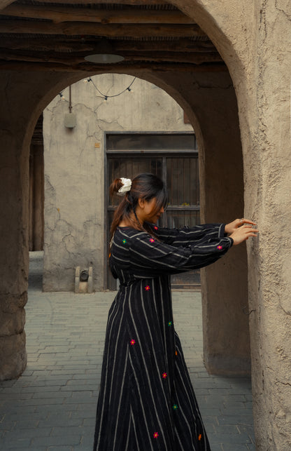 Woman in a black dress with colorful buttons standing in an arched stone doorway.