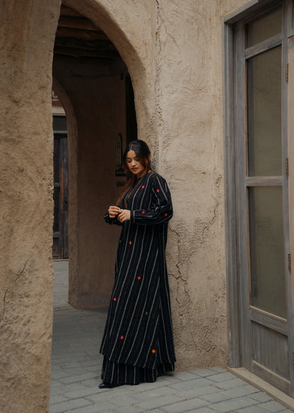 Woman in a long black dress standing in an arched doorway of a stone building.