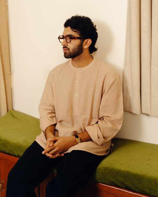 Man sitting on a green cushioned bench wearing glasses and a beige Sand striped shirt.