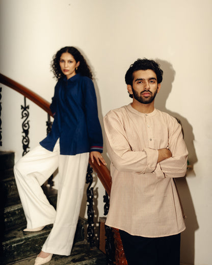 Two people standing on a staircase, one in a Shirt - Blueberry Plain and white pants, the other in a beige striped shirt and dark pants.