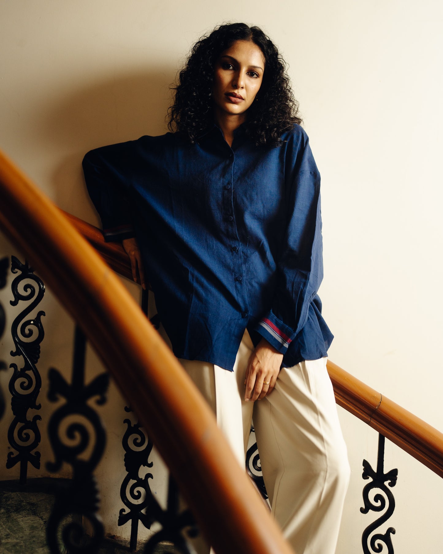 Woman in a blue shirt and white pants standing on a staircase.
