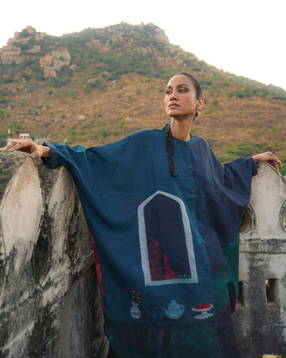 Woman in a blue embroidered dress standing on a stone wall with mountains in the background