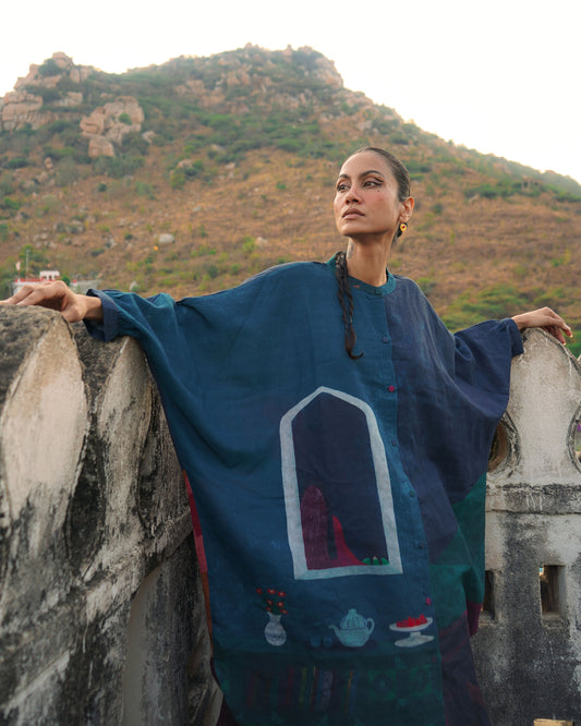Woman in a blue embroidered dress standing on a stone wall with mountains in the background