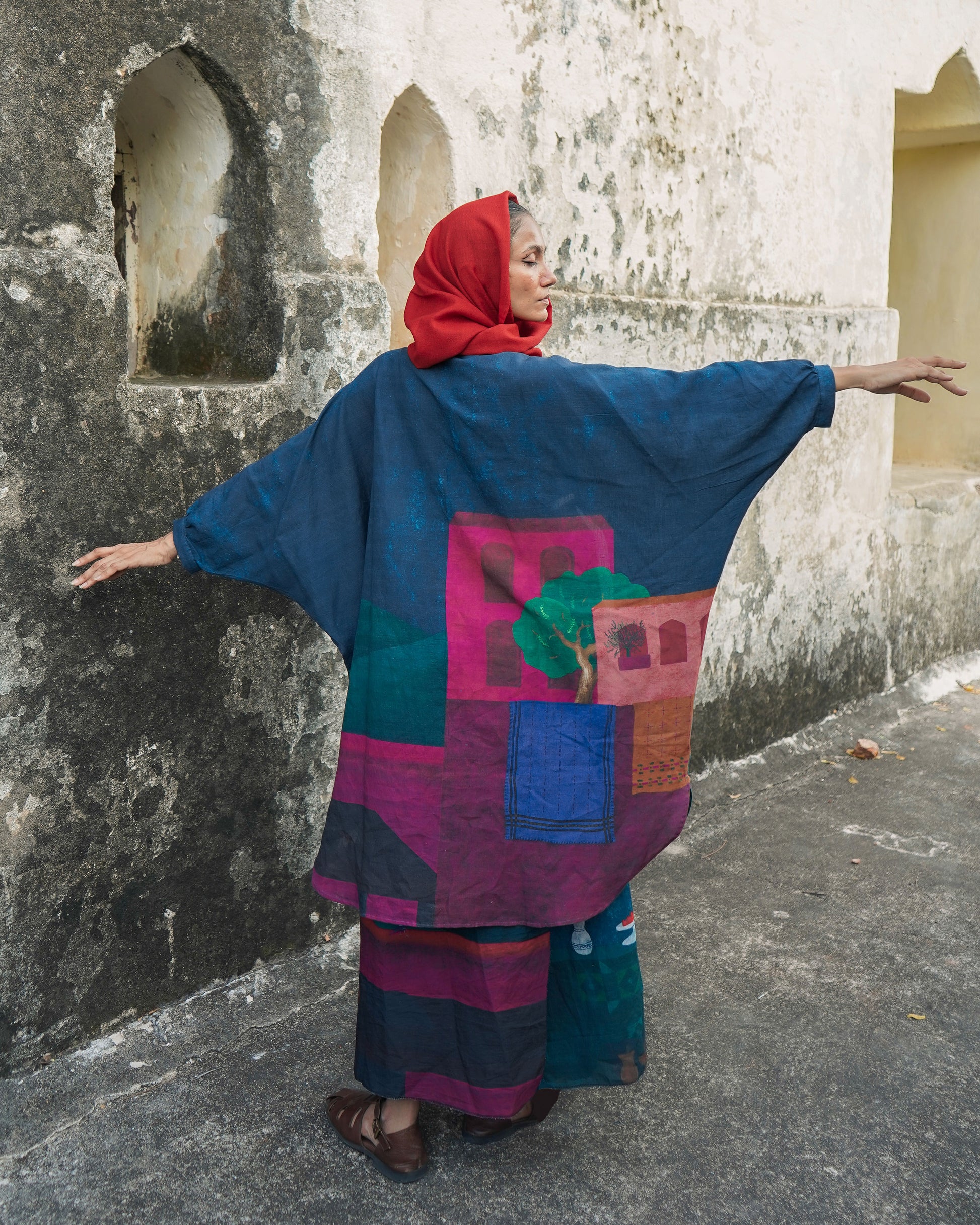 Person wearing a colorful traditional outfit with a patterned shawl against a textured wall.