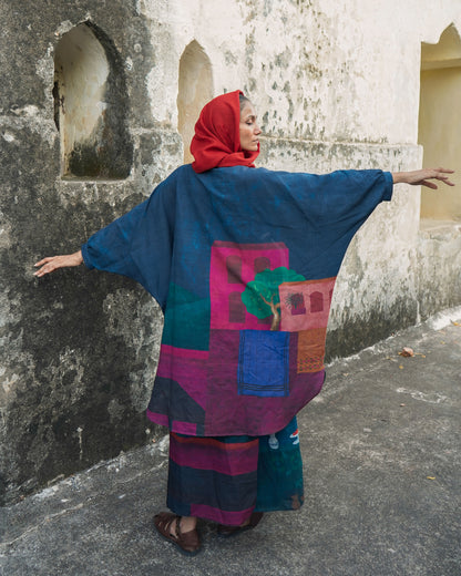 Person wearing a colorful traditional outfit with a patterned shawl against a textured wall.