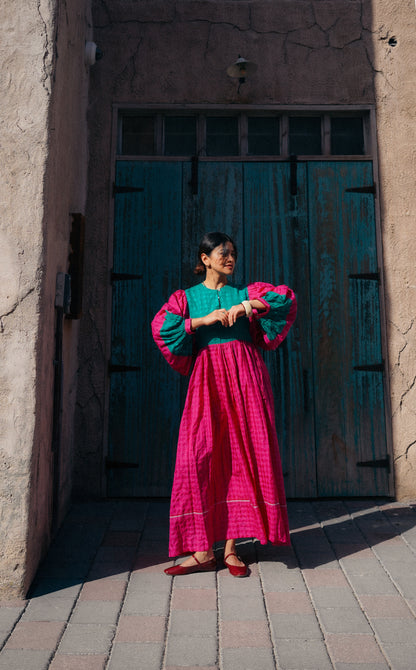 Woman in a colorful outfit standing in front of a textured wall and wooden door.