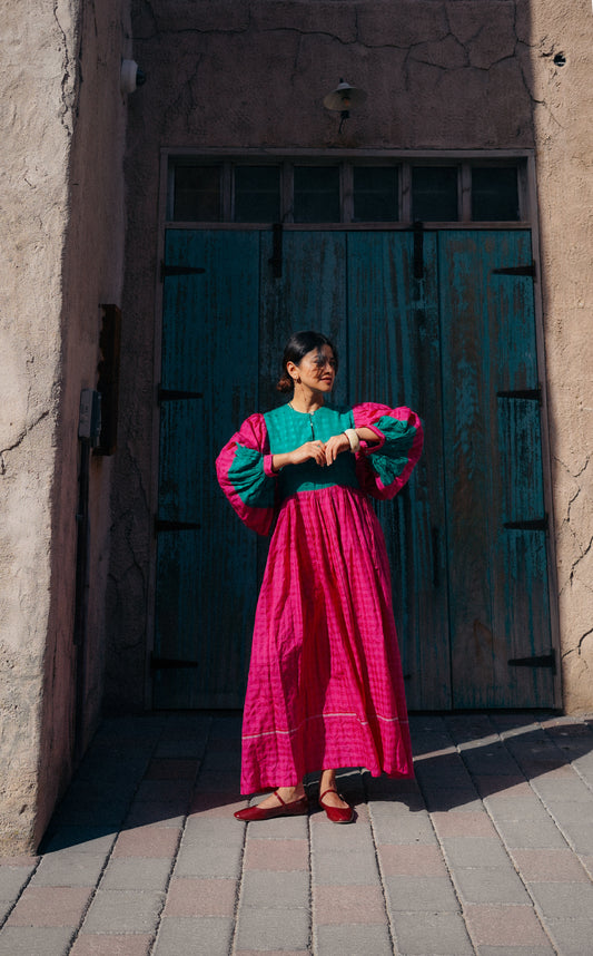 Woman in a colorful outfit standing in front of a textured wall and wooden door.