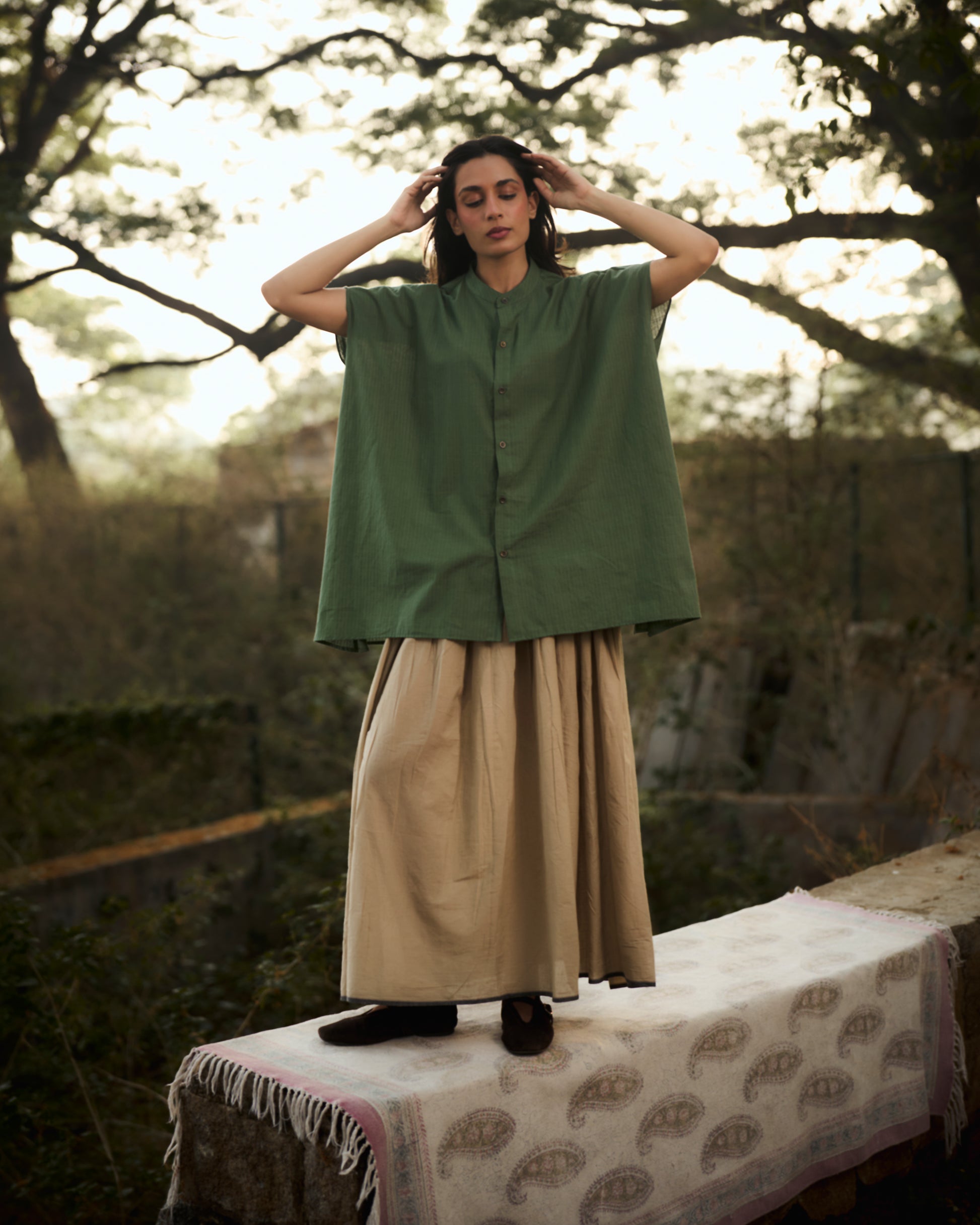 Person wearing a green shirt and beige skirt standing on a table outdoors with trees in the background