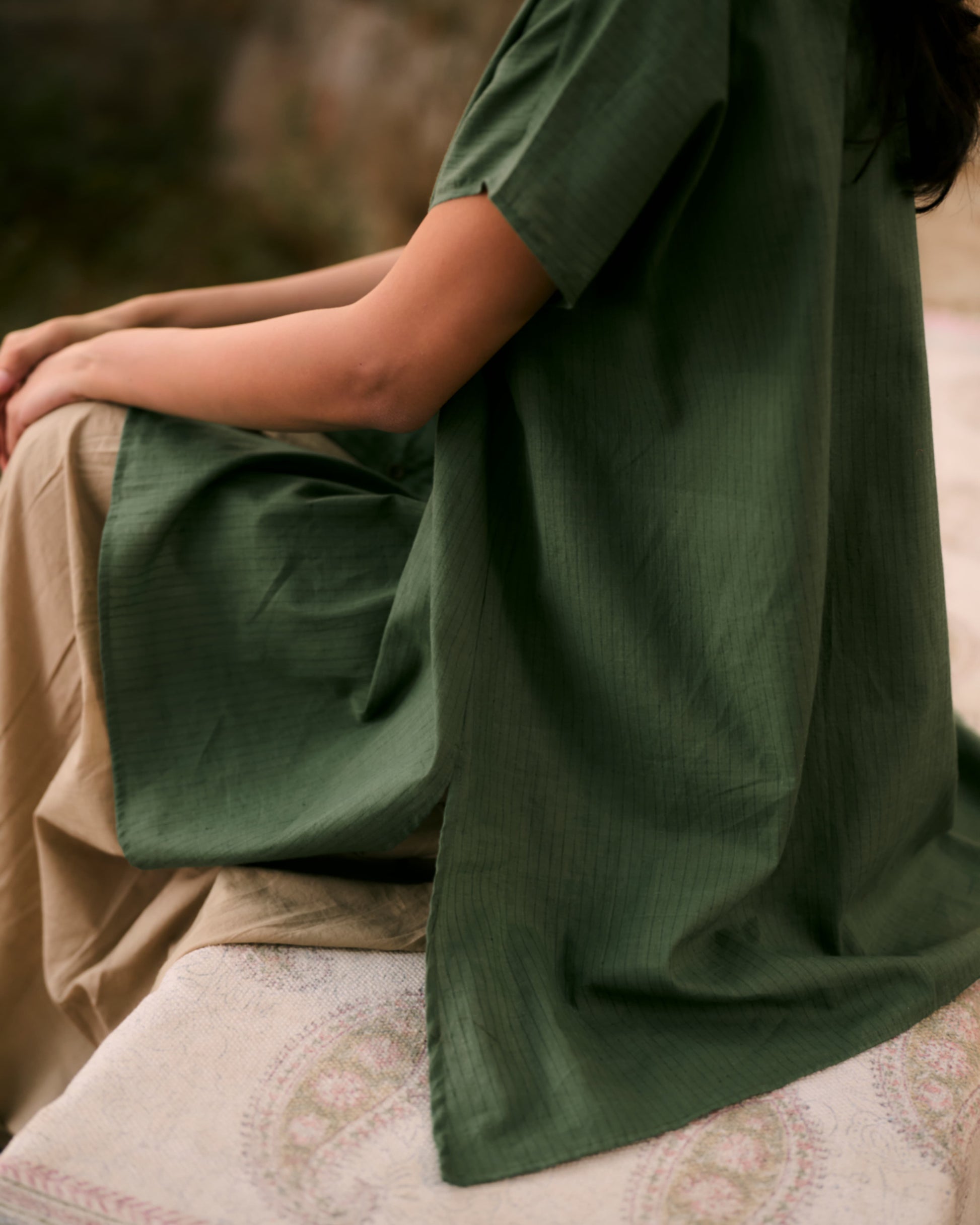 Person wearing a green garment sitting on a textured surface with a blurred natural background