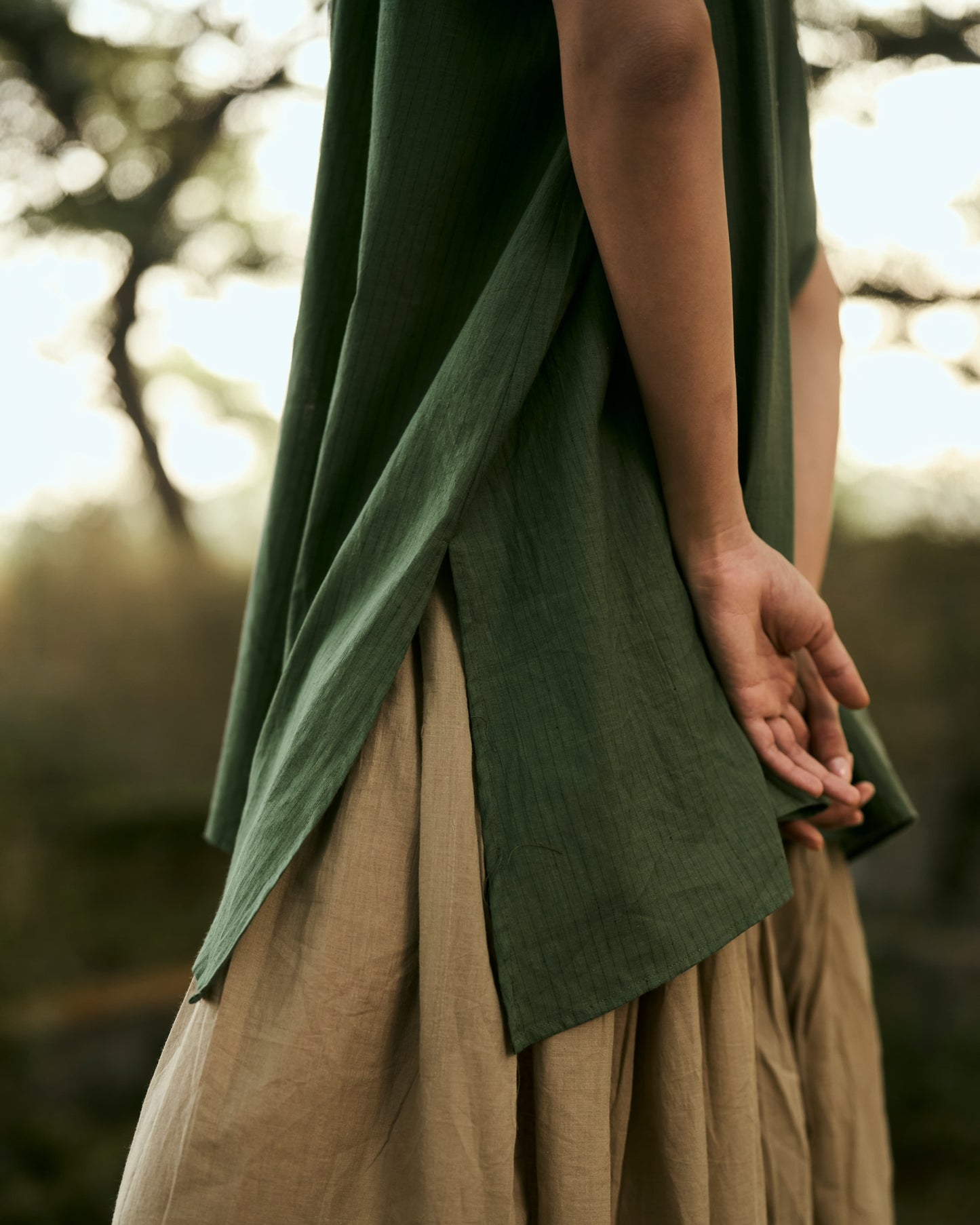 Person wearing a green top and beige skirt with a blurred natural background