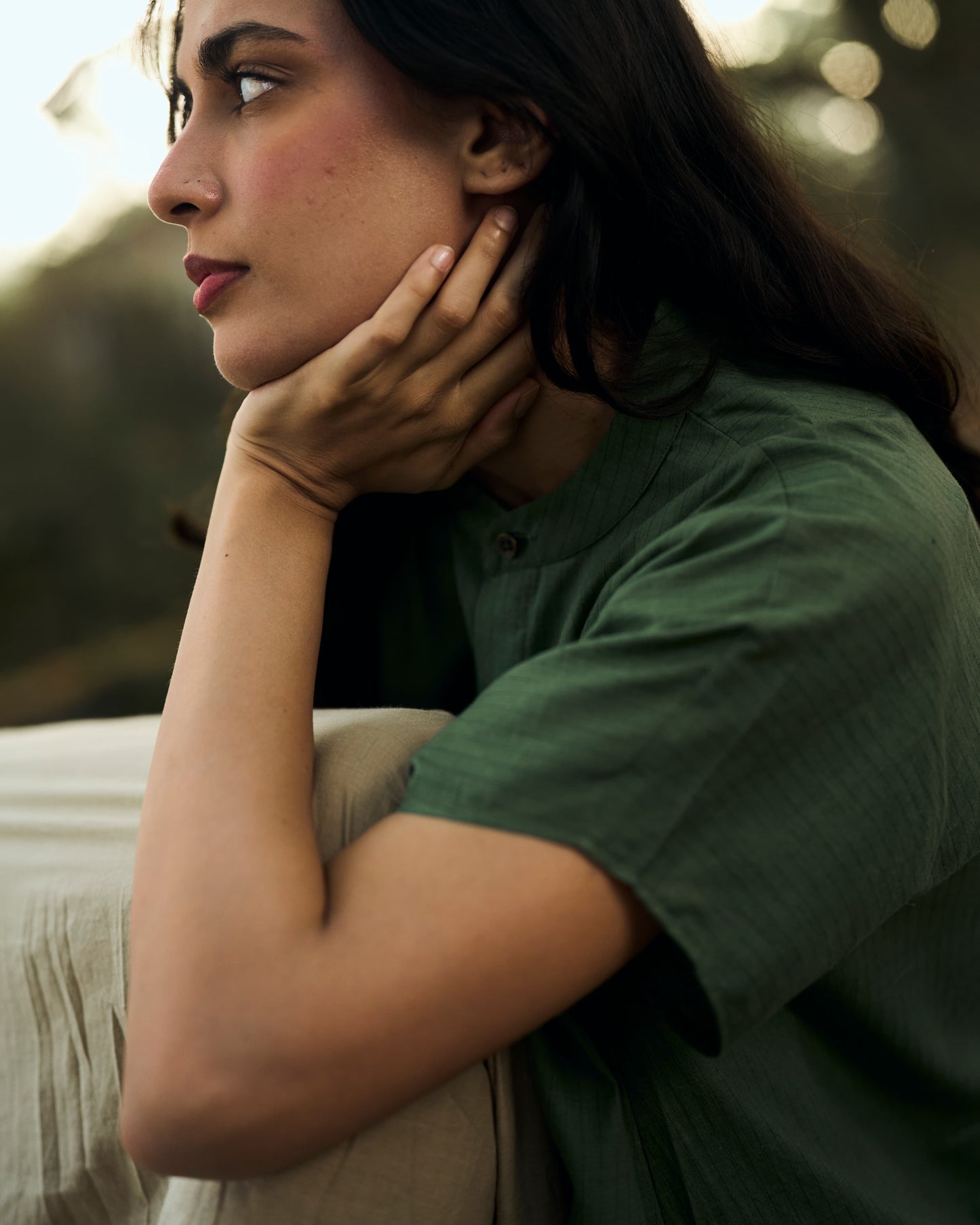 Woman in a green shirt with hand on chin, blurred natural background