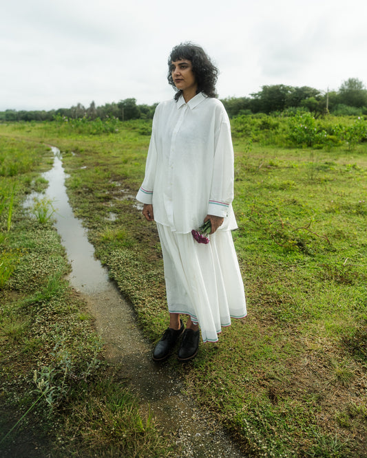 Person in a white outfit standing on a grassy path with water nearby