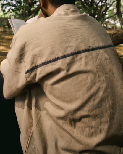 Person wearing a beige jacket with a dark stripe, standing outdoors.